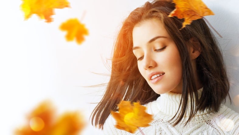 A young woman with smooth skin surrounded by fall leaves